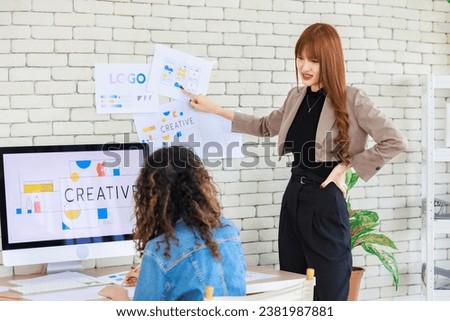 Asian professional successful young female creative graphic designer and colleague in casual fashion suit smiling helping choosing sampling comparing artwork on computer moniter in office workplace.