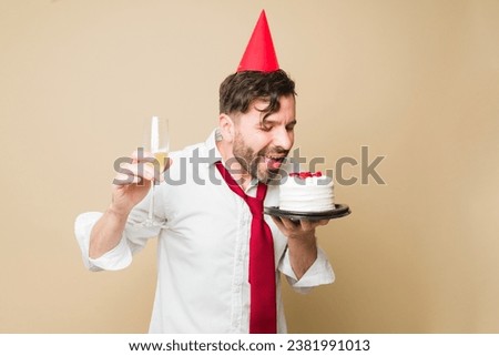 Cheerful happy man eating birthday cake with a party hat and smiling while celebrating a party drinking champagne drinks