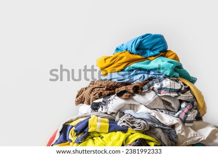 Pile of unfolded dirty clothes for laundry on the chair. Heap of used clothes for donation and recycling. Concept of minimalism, mess and wardrobe cleaning Royalty-Free Stock Photo #2381992333