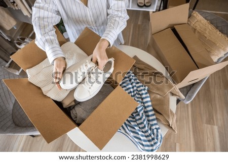 Woman packing clothes and shoes into cardboard box seasonal comfortable storage organize top view closeup. Female with container for wardrobe keep for donation charity online shopping order moving Royalty-Free Stock Photo #2381998629