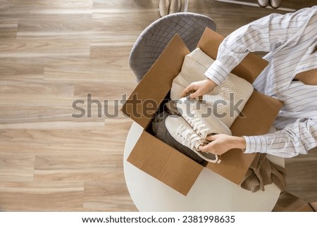 Woman packing clothes and shoes into cardboard box seasonal comfortable storage organize top view closeup. Female with container for wardrobe keep for donation charity online shopping order moving Royalty-Free Stock Photo #2381998635