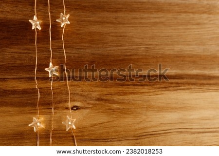 New Year's lights in the shape of stars lie on a wooden background. New Year's garlands glow on a brown background. Background for Christmas. Winter card