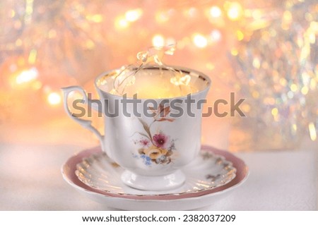 Beautiful coffee cup on a saucer with a small garland on a background with lights. Side view with copy space. Holiday and good morning concept