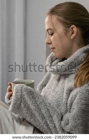 girl sits in bed and warms herself with tea