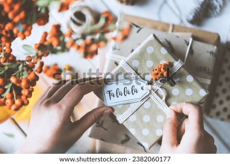 Woman hands gift wrapping christmas presents on wooden table top. Gift with fa la la la tag on top.