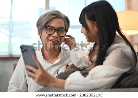 Romantic young couple using mobile phone and listening music new playlist together in living room.
