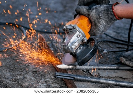 An angle grinder in the hands of a worker sharpens a steel impact tool for a jackhammer. Sparks fly from the power tool blade. Preparation for dismantling a concrete monolithic block outdoors.