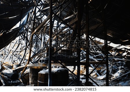 Burnt interiors of ruined factory building after fire, Misfortune in the industry factory, Burning Building, Remains and ashes. Burnt oil tank and Metal sheet roof, steel truss frame - Royalty-Free Stock Photo #2382074815