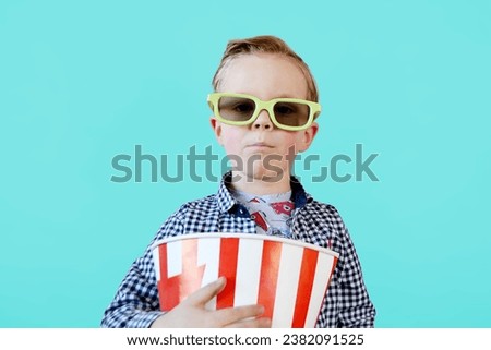 Little cute fun kid baby boy 3-4 years old in red t-shirt holding bucket for popcorn, eating fast food isolated on yellow background. . High quality photo