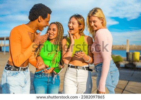 Frontal view of a surprised group of multi-ethnic friends using phone together outdoors Royalty-Free Stock Photo #2382097865
