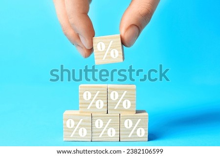 Woman building pyramid of cubes with percent signs on light blue background, closeup