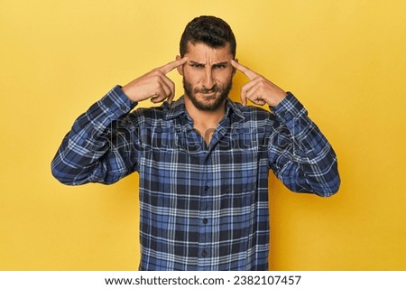 Young Hispanic man on yellow background focused on a task, keeping forefingers pointing head.