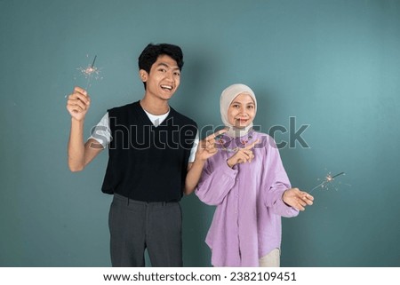 two young asian people are celebrating new year with pointing to right while holding firework in front of blue background