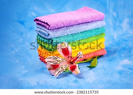 a bright flower and seven rainbow-colored cleaning rags lying on top of each other for upcoming cleansing on a blue background Royalty-Free Stock Photo #2382115735