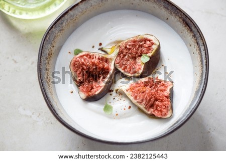 Bowl of greek yogurt topped with torn fig fruits, horizontal shot on a light-beige stone background, middle closeup