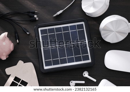 Solar panel, electronic devices, piggy bank and wooden house on wooden background, top view