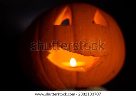 Halloween carved pumpkin with burning candle bright lighting on black background. A bright, colorful orange object on a plain black background with minimal lighting.