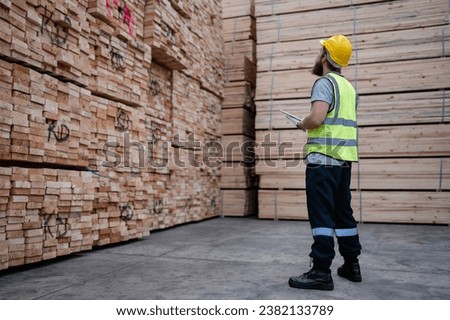 Male engineer standing walking in warehouse examining hardwood material for wood furniture production. Technician supervisor man working on quality control in lumber pallet factory. Worker check stock
