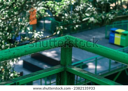 Weathered green railing made of iron with its peeling paint. The background is a soft blur of trees and foliage, enhancing the atmospheric feel of the photo