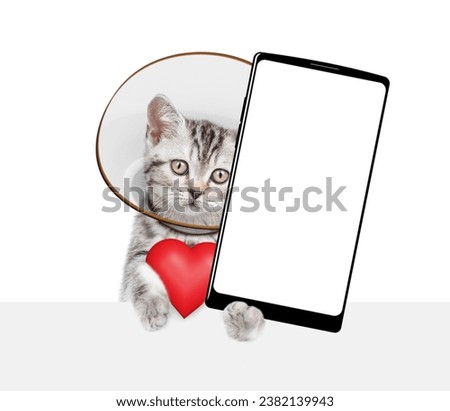 Cute tabby kitten wearing protective cone collar shows red heart and big smartphone with empty screen above empty white banner. Isolated on white background
