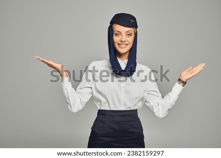 joyful arabian airlines stewardess in headscarf and uniform standing with open arms on grey