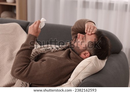 Sick man with tissue lying on sofa at home. Cold symptoms Royalty-Free Stock Photo #2382162593