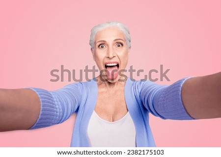 Self portrait of gray haired beautiful smiling funky funny playful old lady wearing casual, grimacing, showing tongue out, isolated over violet background Royalty-Free Stock Photo #2382175103