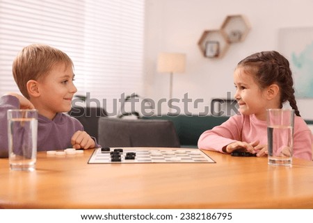 Cute children playing checkers at wooden table in room