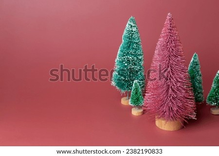 Mini shiny Christmas trees pink and green on pink background. Copy space