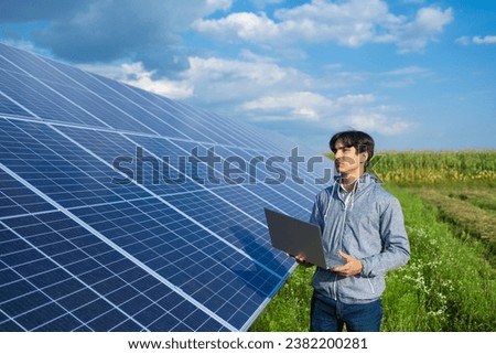 Engineer using a laptop to adjust the inverter of the solar power plant in the meadow on a warm summer's day.