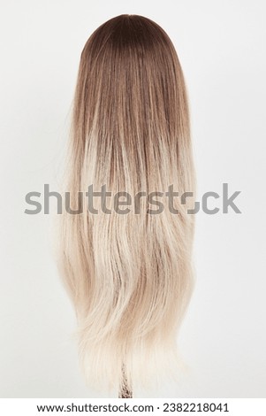 Natural looking blonde wig on white mannequin head. Long hair on the plastic wig holder isolated on white background, back view
