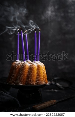 Still life of purple blown out candles on a gugelhupf. Moody style, black background, dessert.
