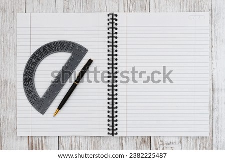 Ruled line paper page notepad with pen and protractor background on weathered desk for notes or math 