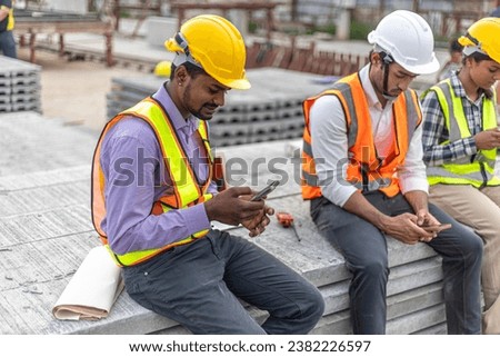 A group of civil engineers checking their smartphones for information or connecting with social media when taking a break at a construction site