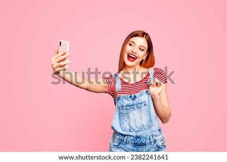 Portrait of nice vivid red straight-haired excited happy smiling young girl with opened mouth taking self picture, isolated over blue background