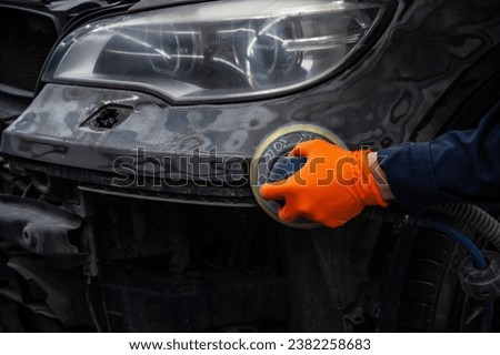 A mechanic sands the putty on a car body with a machine. Repair after an accident.  Royalty-Free Stock Photo #2382258683