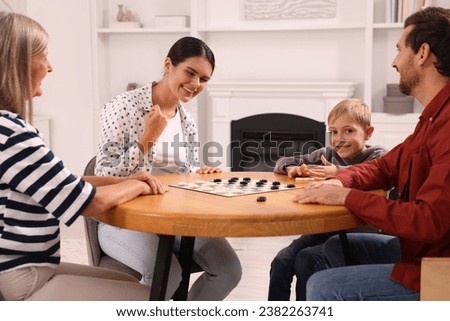 Family playing checkers at wooden table in room. Mother enjoying winning