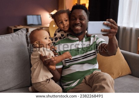 Portrait of happy Black father taking selfie photo with two children at home and making family memories