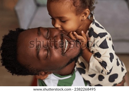 Close up portrait of Black little girl kissing father on cheek and smiling happily enjoying playtime together