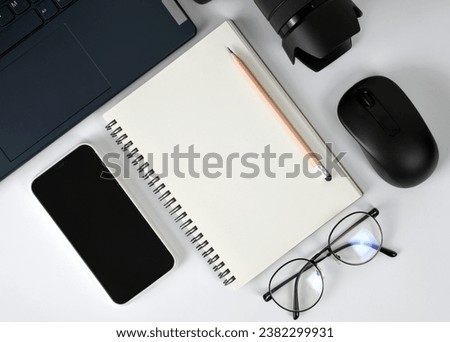 Minimalist style white working top table flat lay with blank notebook pages surrounded by modern lifestyle gadgets electronic devices