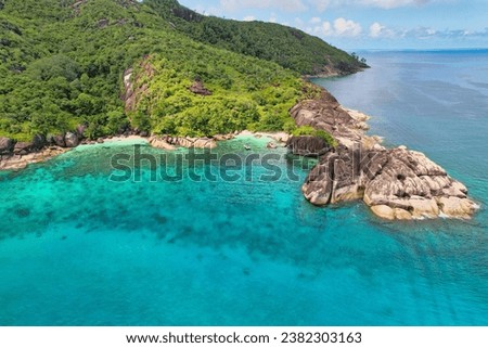 Drone shot of Anse du riz, rice beach beach, transparent sea, lush forest and granite stones, docked boat, Mahe, Seychelles 
