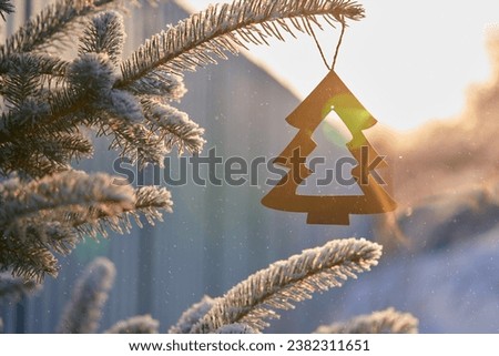 Christmas decoration - Christmas tree cut out of plywood on snow-covered branch of fir tree outside in sunlight. Copy space.                               