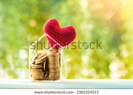 House model and gold coin and red heart put on the wood on sunlight in the public park, The buying a new real estate as a gift to family or the one loved concept.