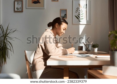 Minimal side view portrait of young African American woman writing in notebook at home with sun rays, copy space Royalty-Free Stock Photo #2382339379