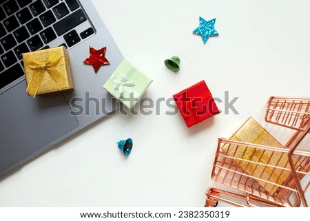 Shopping cart, gift boxes, laptop on the white background. Christmas shopping online. Top view.