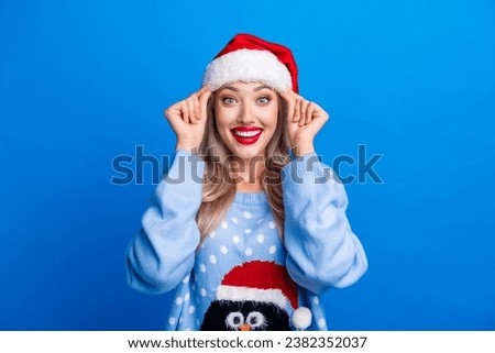 Photo portrait of attractive blonde young woman fix headwear excited dressed penguin sweater x-mas hat isolated on blue color background