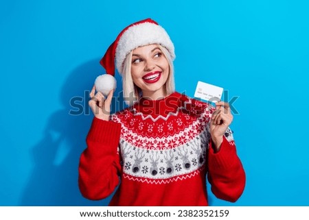Portrait of attractive minded person hold hat pompom debit card look empty space dream x-mas eve sweater isolated on blue color background