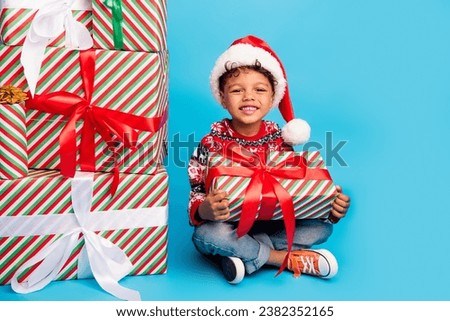 Photo of good mood small boy dressed ornament sweater santa hat sit hands hold surprise on christmas isolated on blue color background