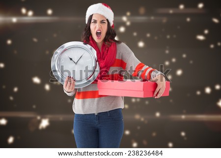 Surprised brunette holding a clock and gift against blurred lights
