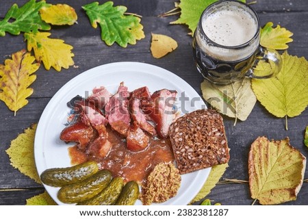 Close up picture of the unboned slowly roasted smoked pork knuckle served with rye bread, rustic style mustard, pickles and mug of dark beer. Autumn specialty from Czech republic, Bavaria or Austria.